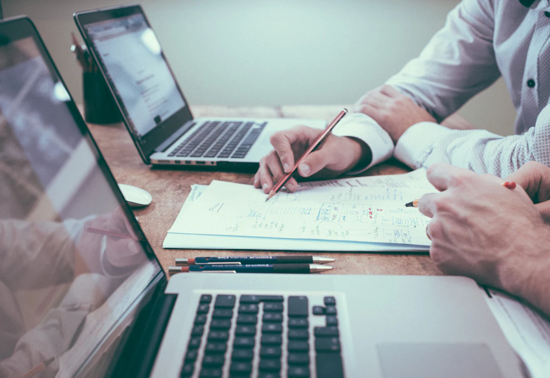 Two people reviewing business paperwork at a desk with laptops
